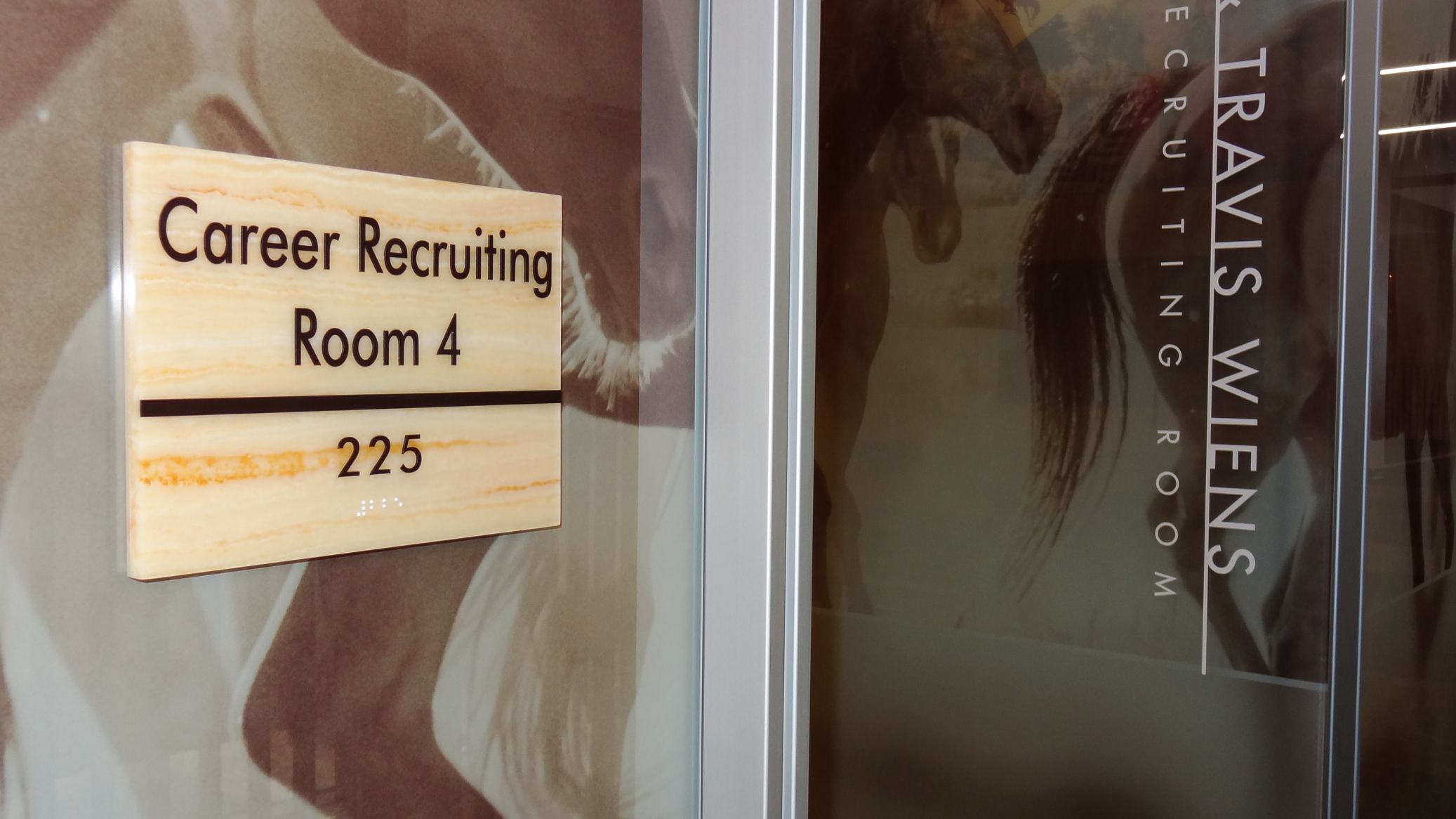 A close-up of a door with a sign reading "Career Recruiting Room 4" and the room number "225" in Braille. The door also has part of another sign with partially visible text including the name "TRAVIS WIENS" and "RECRUITING ROOM.