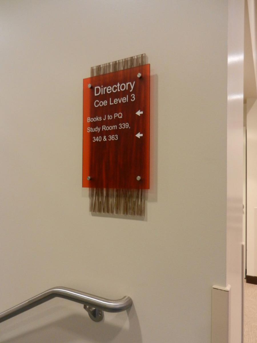 A directory sign on a wall at Coe Level 3 indicating the location of books J to PQ and study rooms 339, 340, and 363. The sign is red with white text and is mounted on a decorative backing. A handrail is visible on the left.
