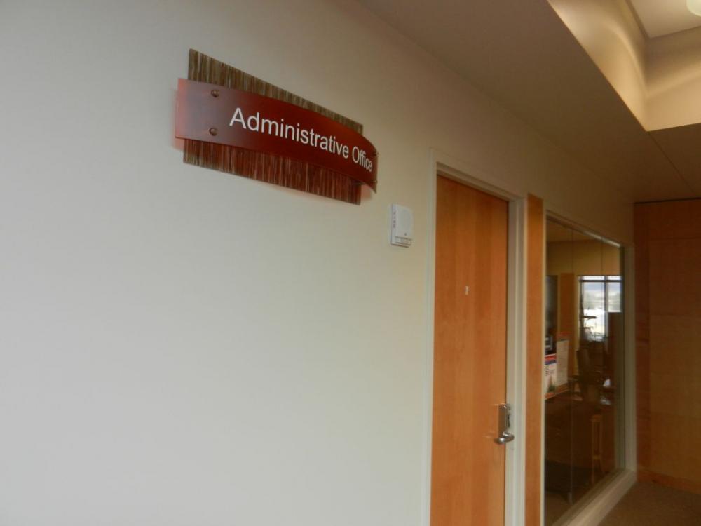 A hallway leads to an office with a wooden door and a glass wall. Above the wooden door, there's a sign that reads "Administrative Office." The space inside the office is visible through the glass wall.