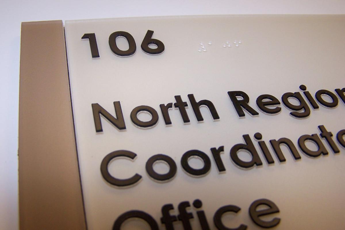 A close-up of a room sign with the number "106" in large black numbers at the top left. Below it, in smaller black letters, are the words "North Region Coordination Office." The sign has braille characters above the text.