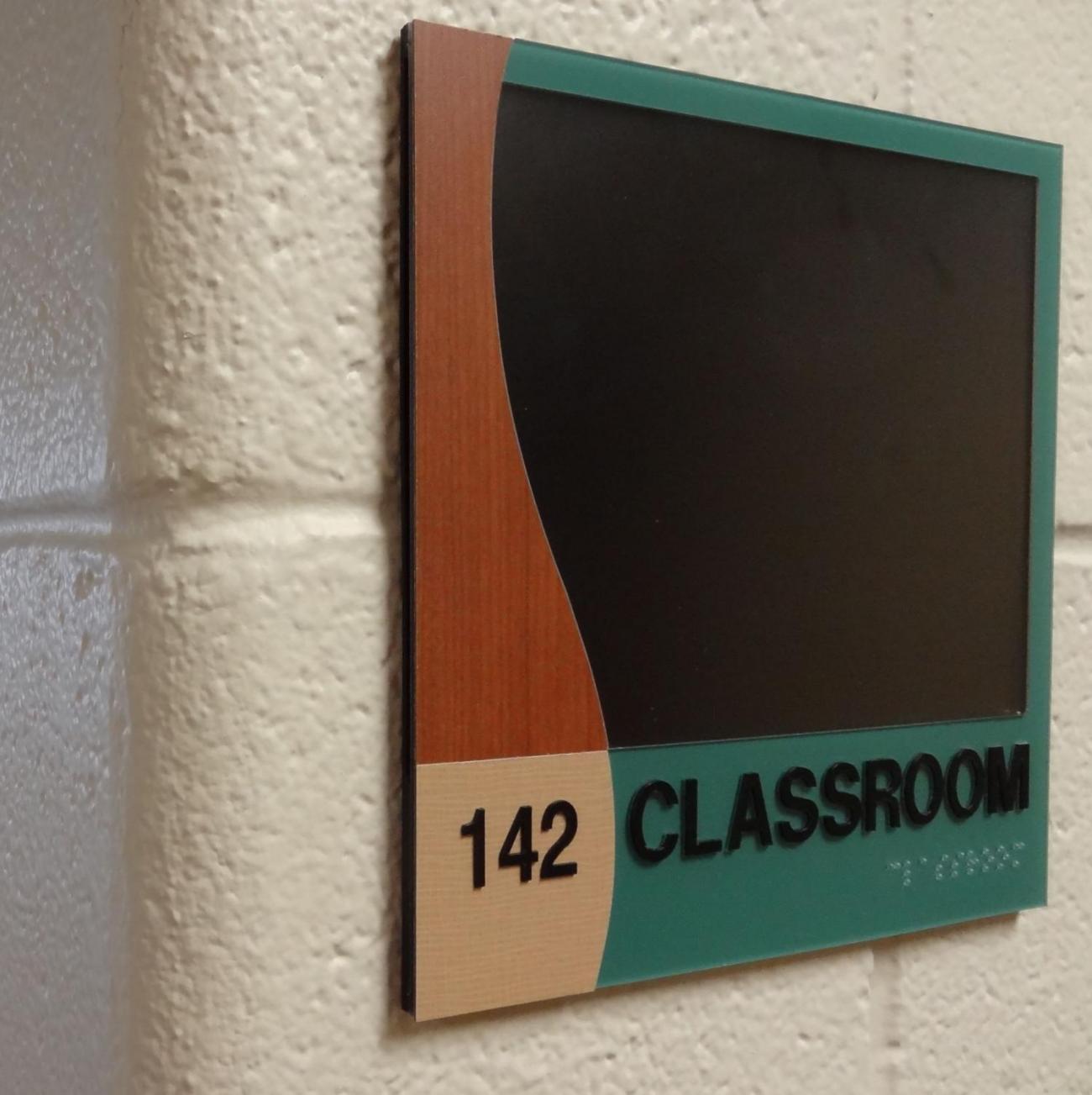 A sign is marked "147 CLASSROOM" with a decorative black and wood-colored design at the top.   Braille writing is included in bottom right corner.