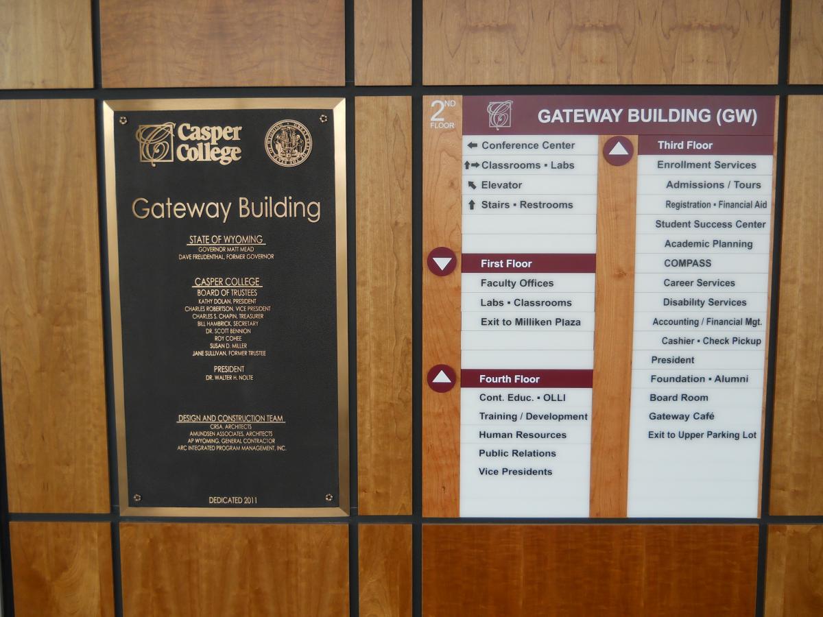 Wall in the Gateway Building at Casper College featuring a bronze plaque on the left and a directory board on the right. The directory lists various departments and their locations across four floors, including classrooms, labs, and student services.