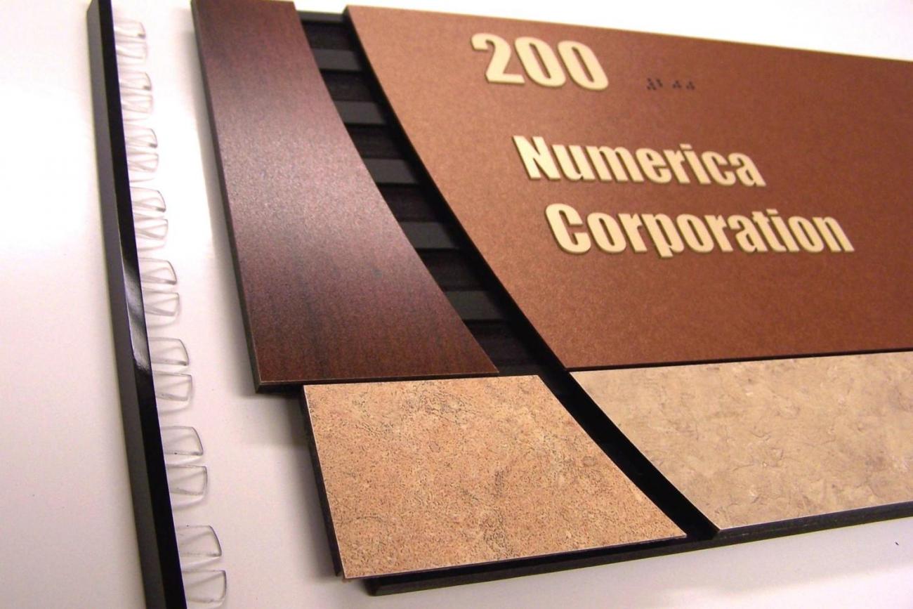 A close-up view of a corporate office sign for Numerica Corporation, featuring the number 200 on a brown, beige, and black background. The sign has a modern design with layered, diagonal cuts and contrasting textures.