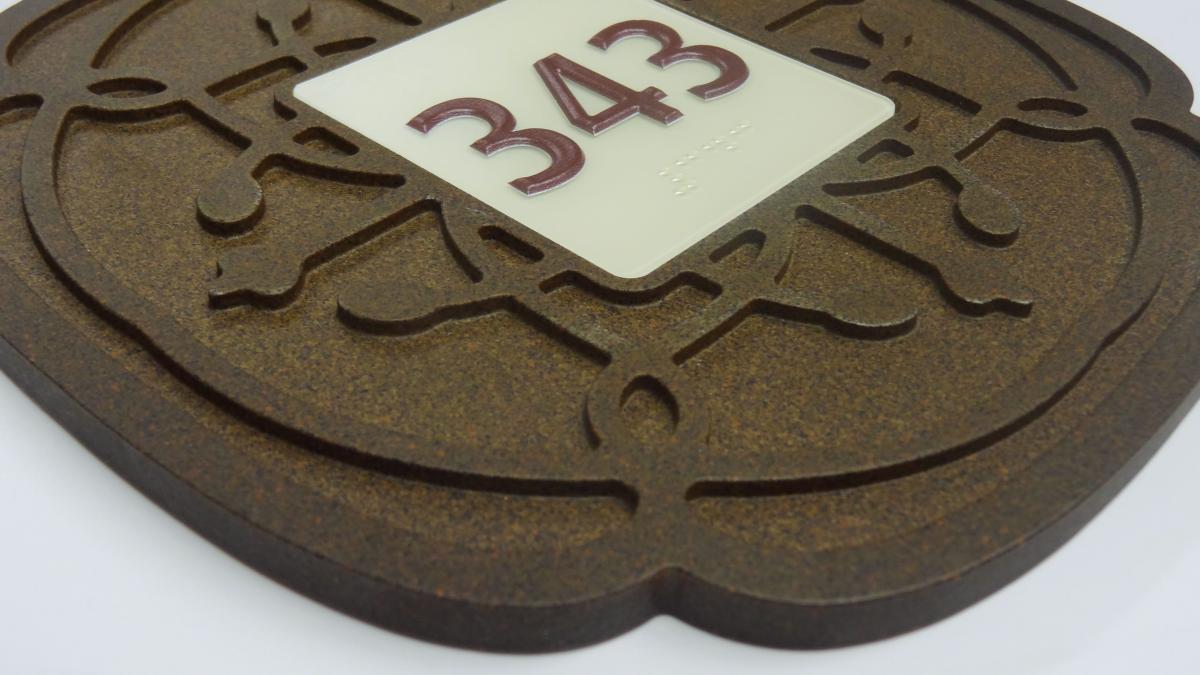 A close-up of a decorative room number plaque, displaying the number "343" in raised, dark red characters on a translucent white square. The plaque features an ornate, brownish pattern that adds an elegant touch to the design.