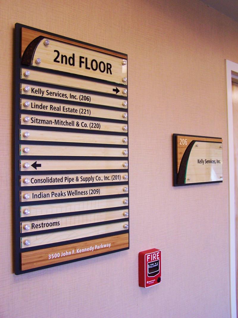 Directory sign for the 2nd floor displaying offices: Kelly Services, Inc. (206), Linder Real Estate (221), Sitzman-Mitchell & Co. (220), Consolidated Pipe & Supply Co. Inc. (201), Indian Peaks Wellness (209), and Restrooms. Fire alarm and Kelly Services sign.