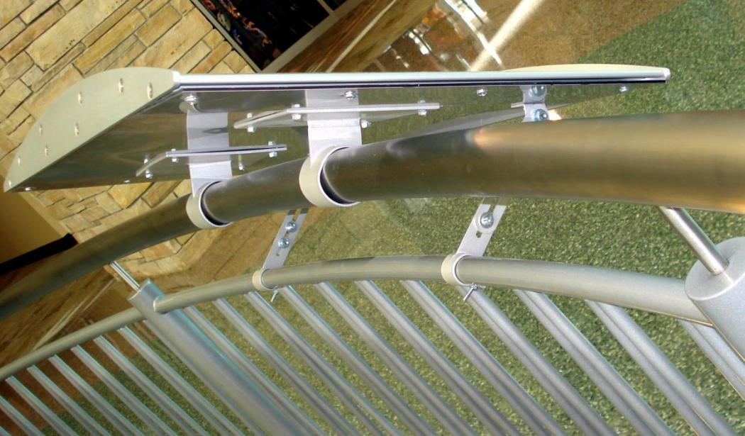 A metal railing with a mounted flat rectangular sign bracket fixed on top in a brightly lit indoor space, featuring green patterned flooring and stone wall accents in the background.