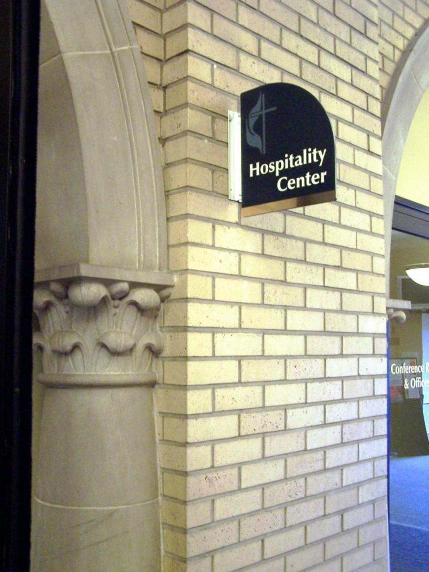 A brick wall with an arched detail and a sign that reads "Hospitality Center." The arch has decorative stonework, and another sign in the background reads "Conference & Office."