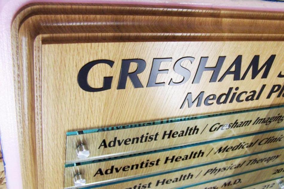 A wood and metal directory sign for a medical professional building. The top part has bold text that says "GRESHAM Medical Professionals". Individual sections underneath list different health services, including Adventist Health, Gresham Imaging, and Medical Clinic.