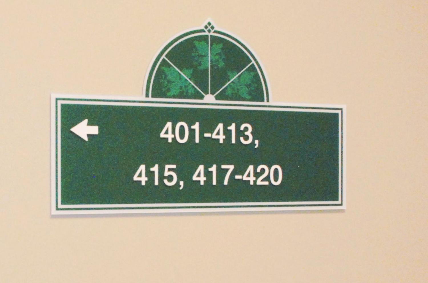 A green wall sign with white text and an arrow pointing left indicates rooms 401-413, 415, and 417-420. The top of the sign has a semicircular decorative element with a green leafy design.