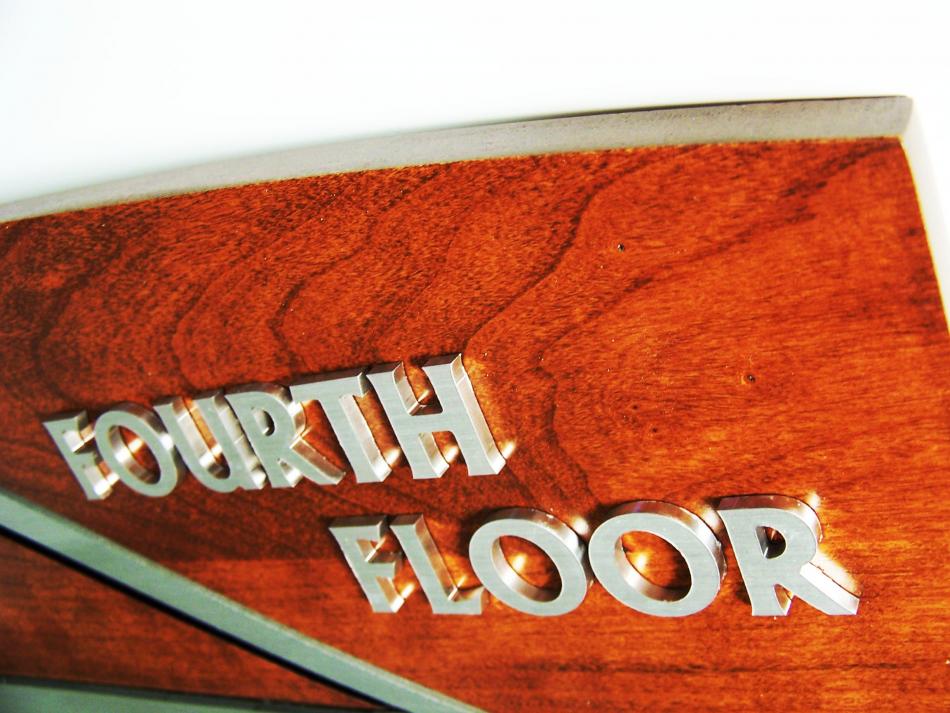 Close-up image of a wooden sign with metallic lettering that partially reads "FOURTH FLOOR." The focus is on the top edge of the sign, highlighting its curved design and polished wood finish.