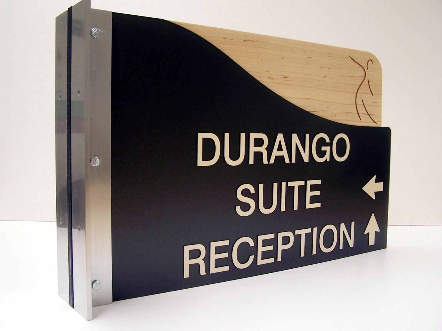 A black and wooden directional sign with a metal bracket. The sign reads "DURANGO SUITE" with an arrow pointing left and "RECEPTION" with an arrow pointing up. The top right corner features a subtle line drawing of a figure.