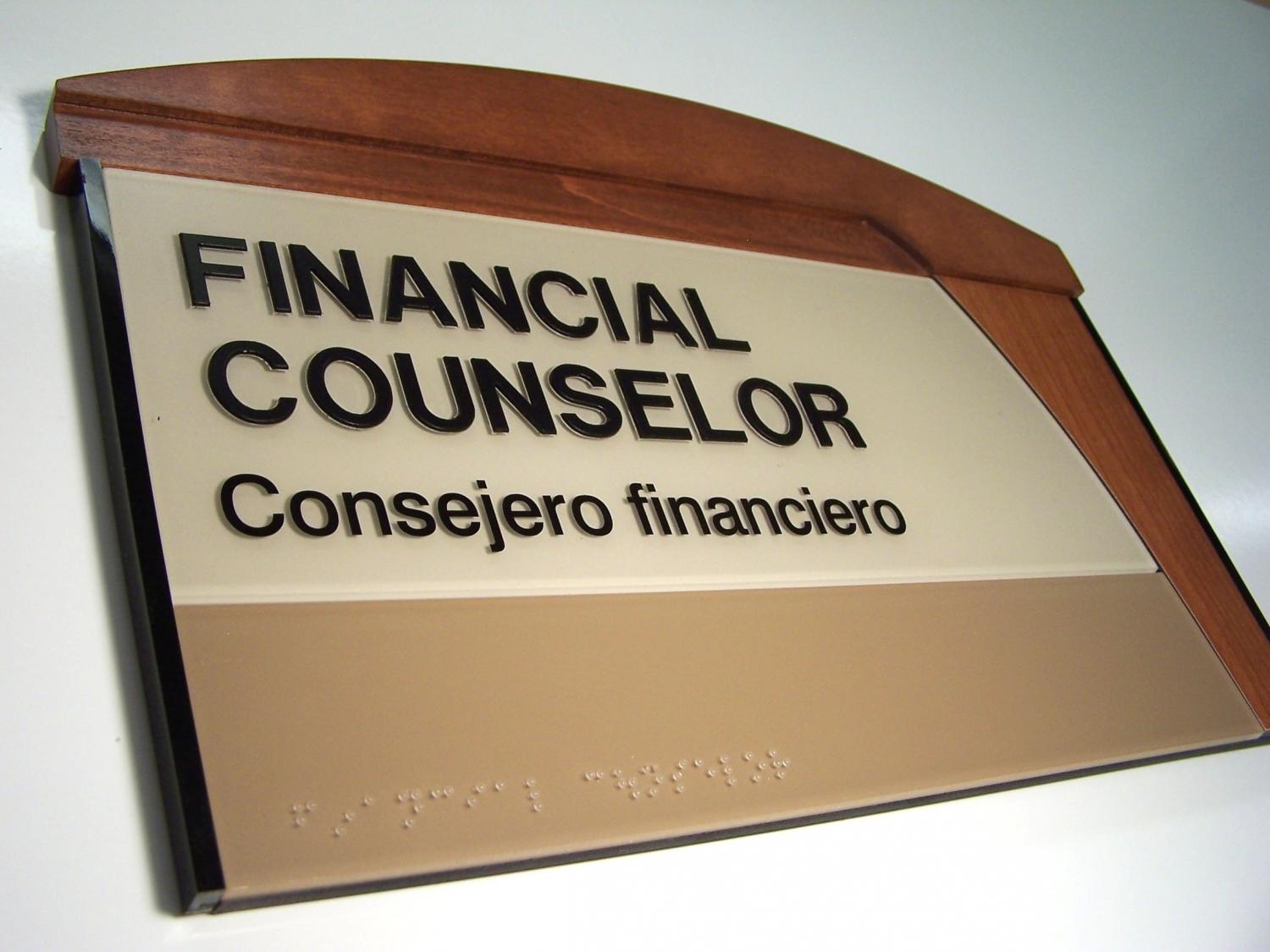 A sign on a wall reads "FINANCIAL COUNSELOR Consejero financiero" with Braille text beneath. The sign has a wooden top border with a beige and brown color scheme.