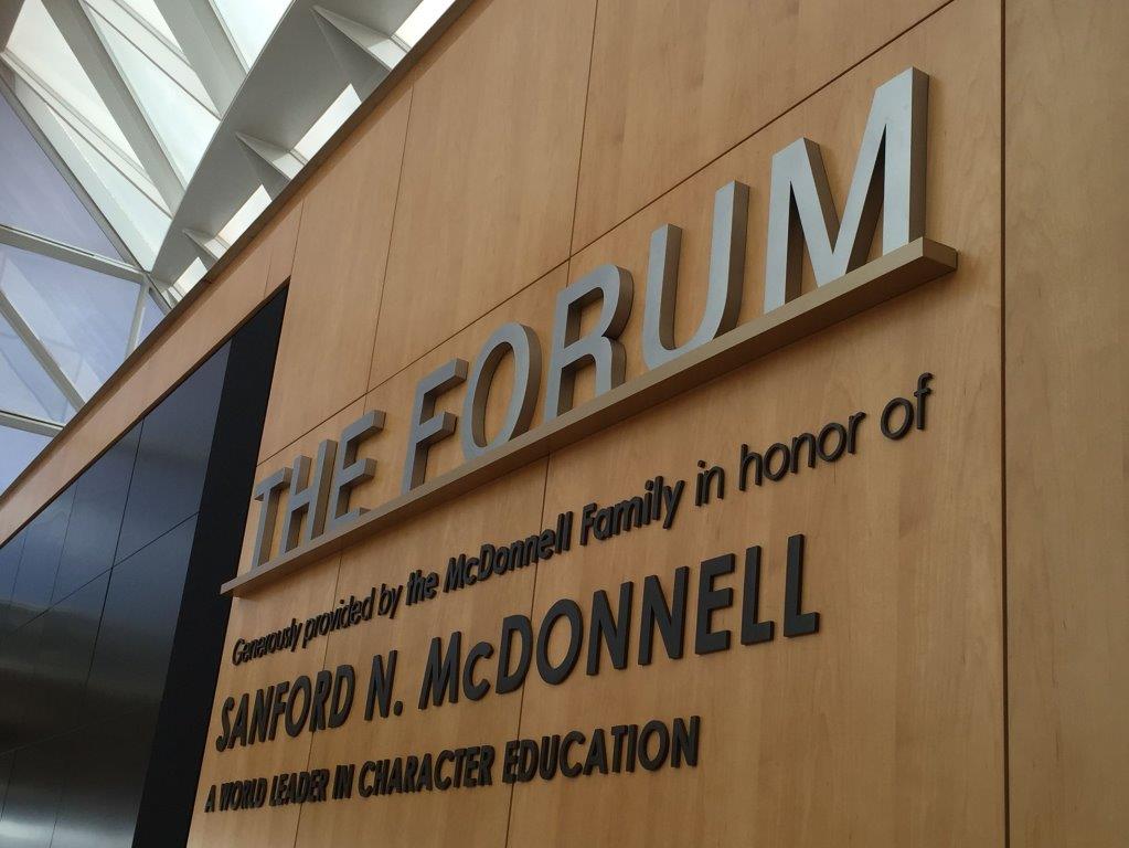 A wall with large text reading "THE FORUM," followed by smaller text stating, "Generously provided by the McDonnell Family in honor of Sanford N. McDonnell, a world leader in character education." The wall is wooden, and the letters are prominently displayed.
