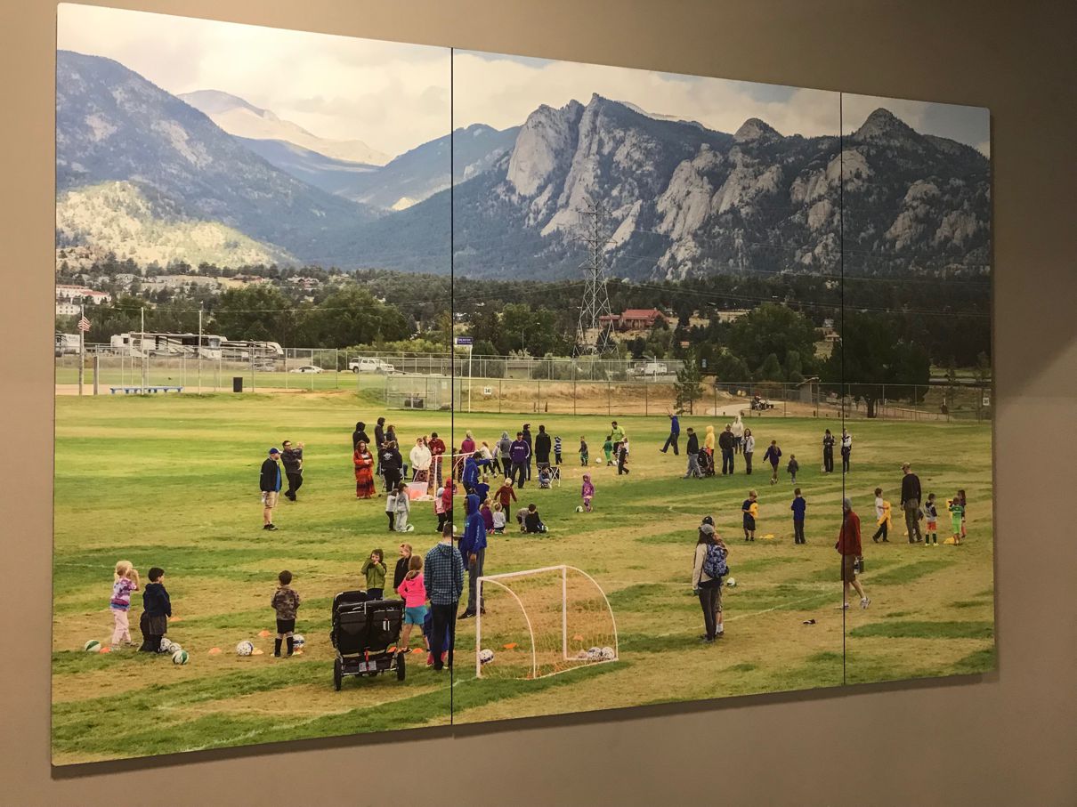 A hallway with a large multi-panel photograph on the wall depicting people playing sports on a field with mountains in the background.