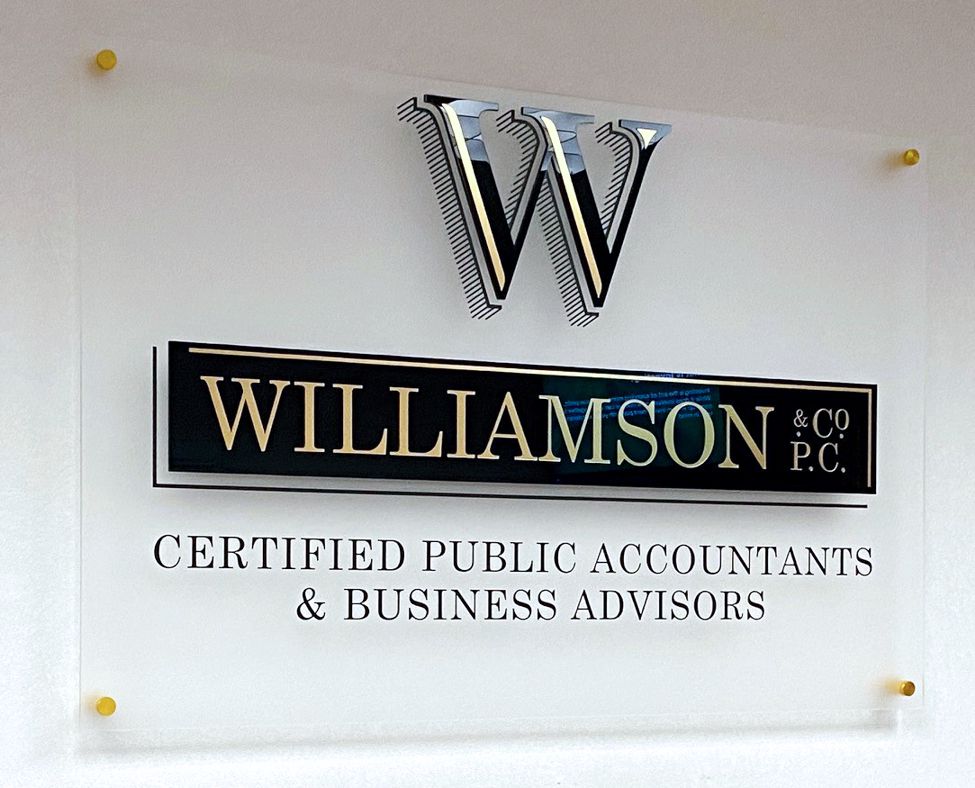 A sign on a wall reads "Williamson & Co PC, Certified Public Accountants & Business Advisors" below a metallic logo with the letter "W".