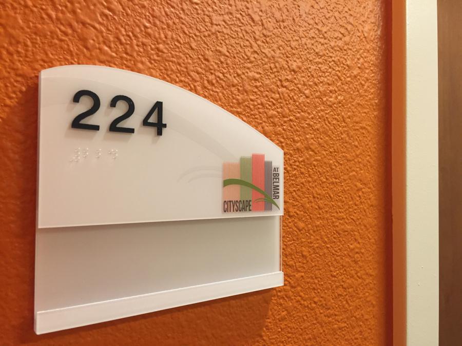 Room sign for "224" on an orange-textured wall in a building, with Cityscape and Newland logos. Braille is present beneath the room number.