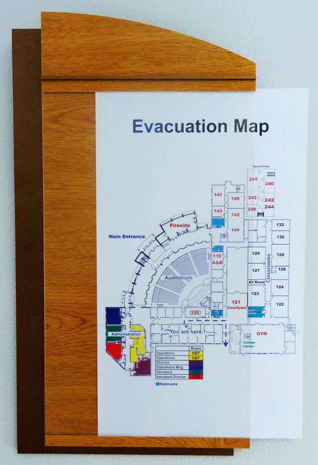 A wall-mounted evacuation map framed in wood shows a detailed layout of a building with various rooms numbered. The areas are color-coded, and exits are marked. The map has a title "Evacuation Map" at the top.