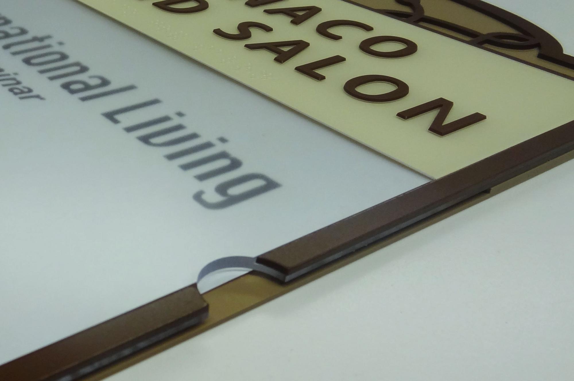 A close-up of a sign displaying partially visible text that reads "National/Living" on the left side and "MONACO" atop "SALON" on the right side, with metallic accents around the edges. The background is a neutral, light-colored surface.