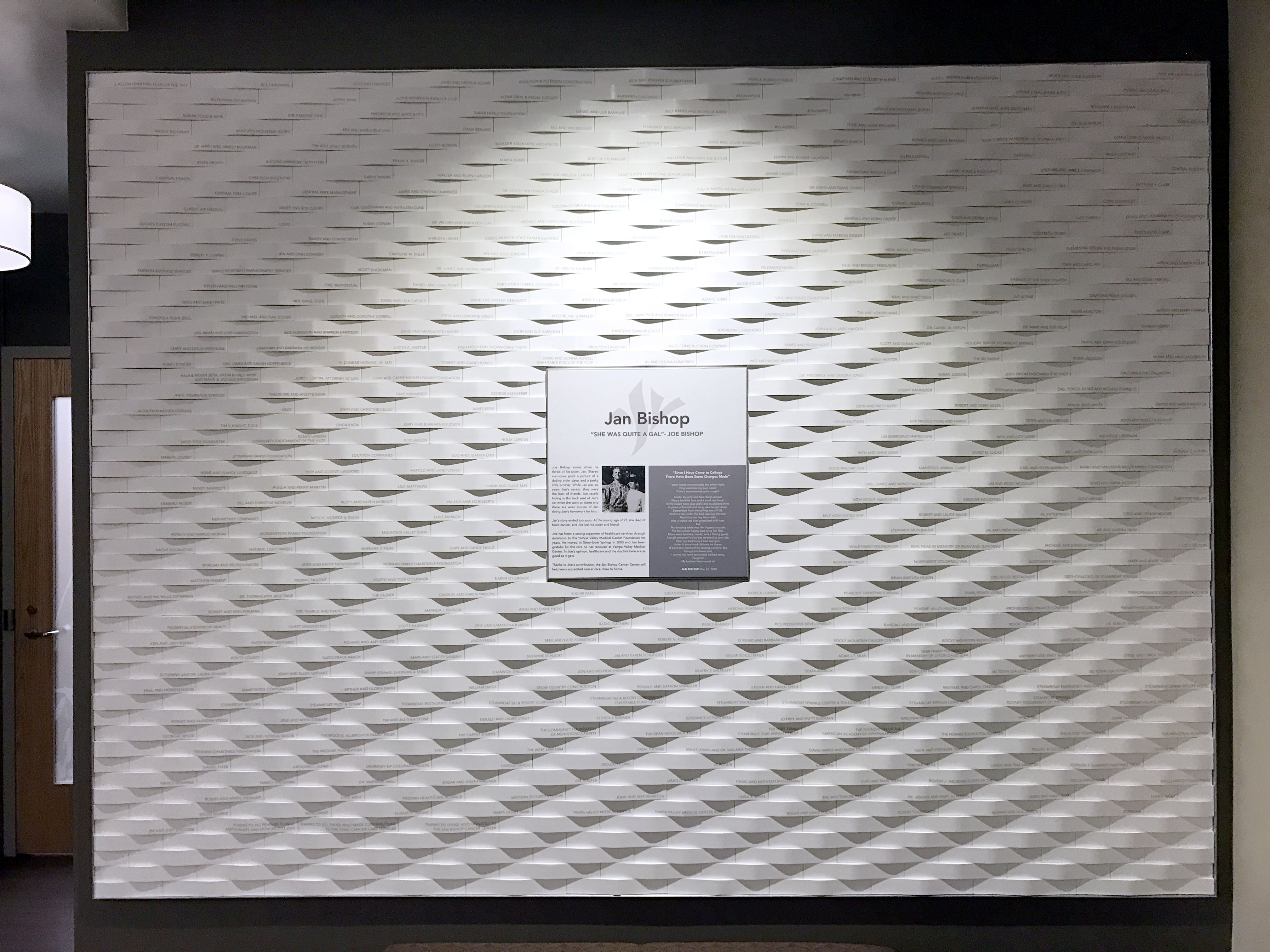 A textured white wall with a diamond pattern has a plaque in the center. The plaque features a photo of a person and text about Jim Bishop, though the details are not fully readable in the image.