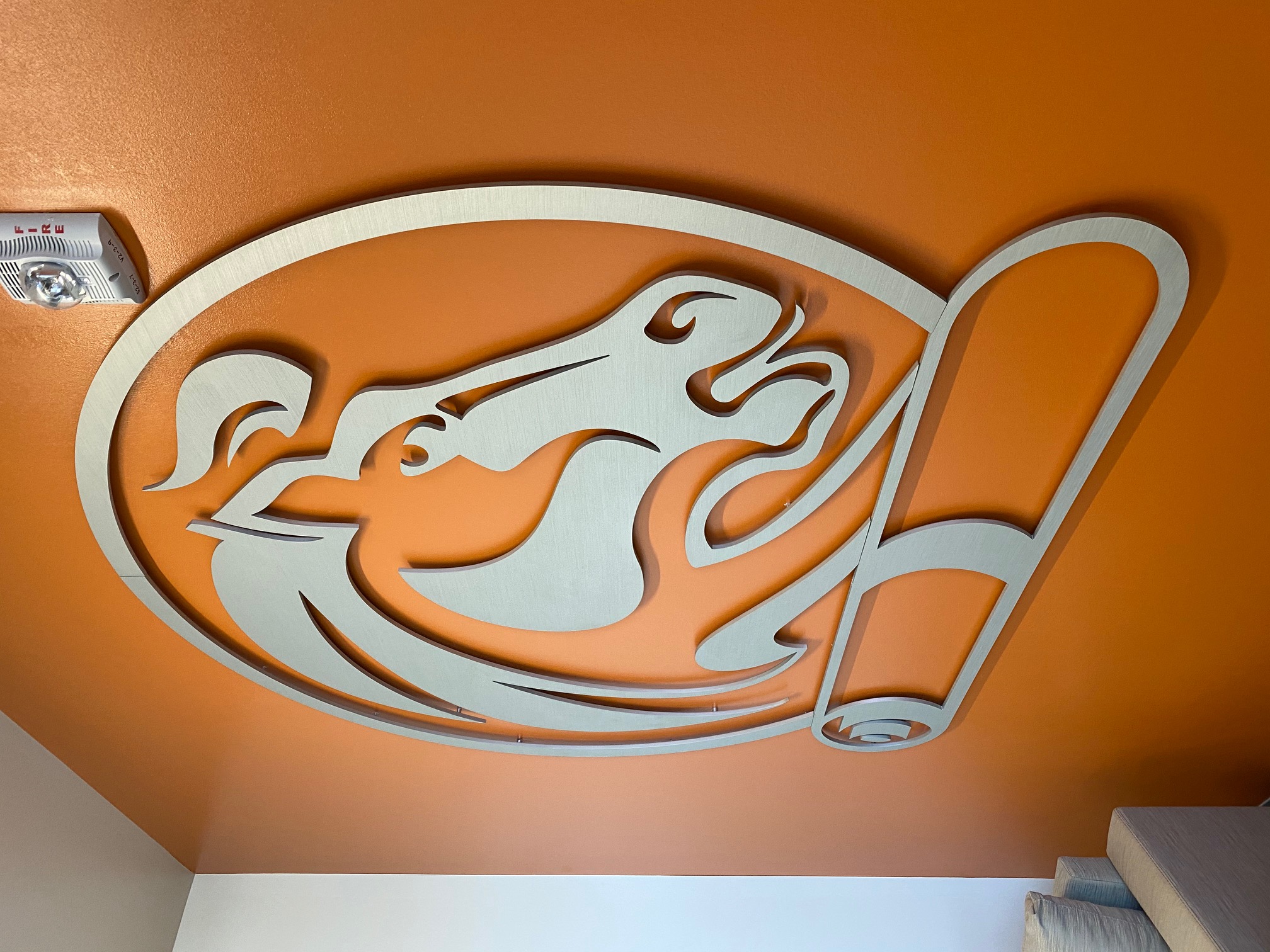 A wall adorned with an orange matte finish displays a stylized horse logo above a scroll. The logo is prominently centered. This is a closeup.