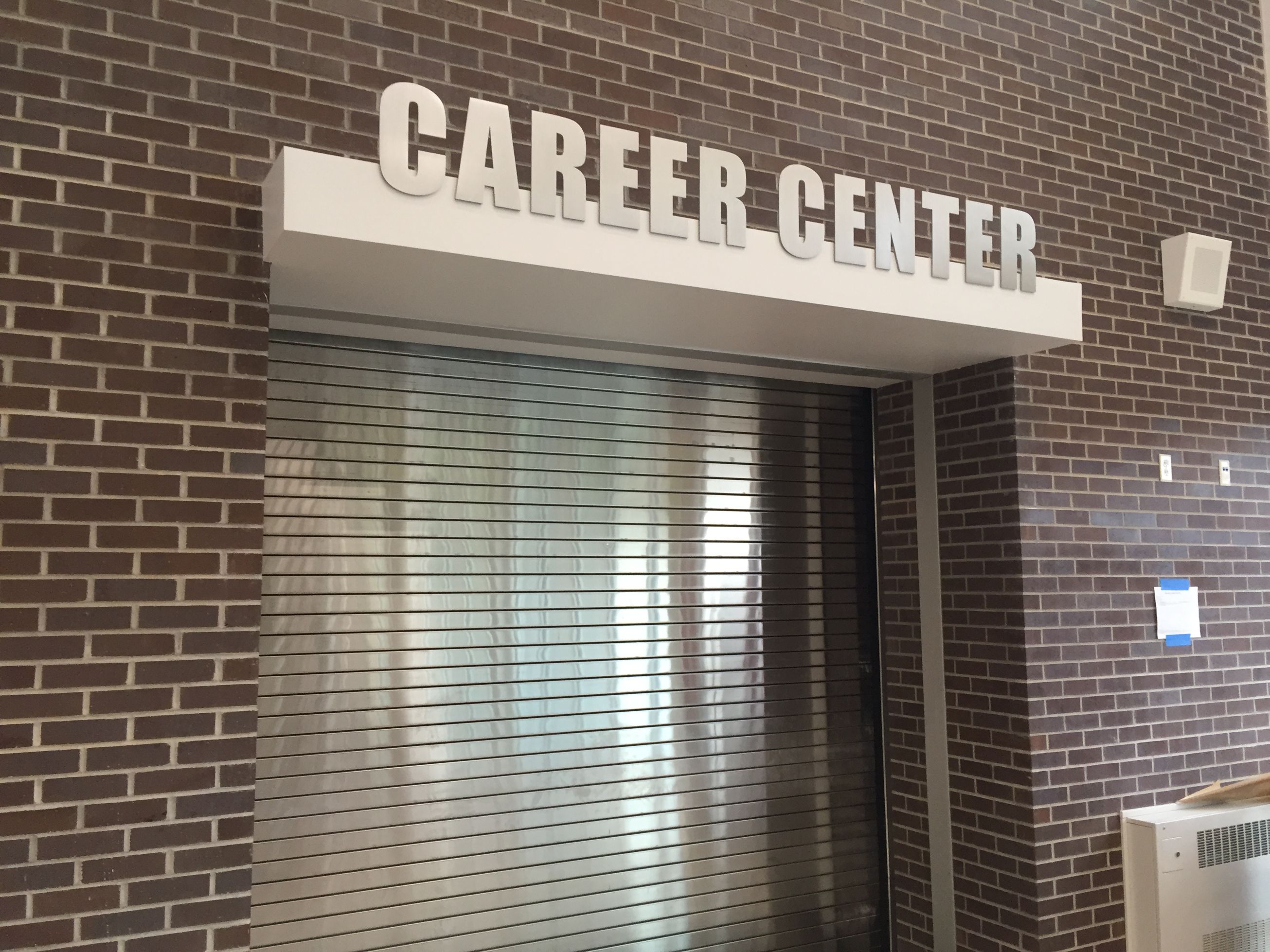 A closed Career Center with a silver metal rolling shutter door, set in a brown brick wall. The white sign "CAREER CENTER" is prominently displayed above the entrance.