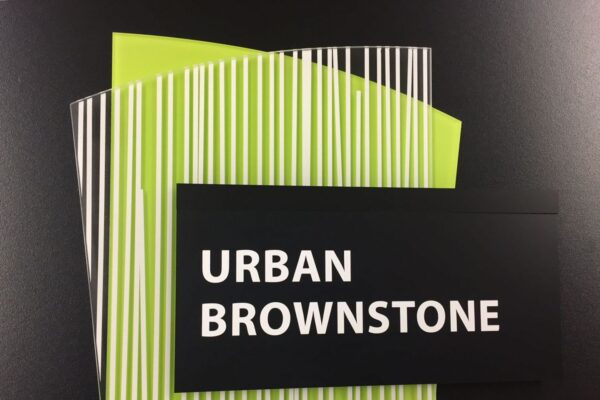 A rectangular black card with the text "URBAN BROWNSTONE" is placed on top of two lime green papers with black and white vertical stripes. The items are against a solid black background.
