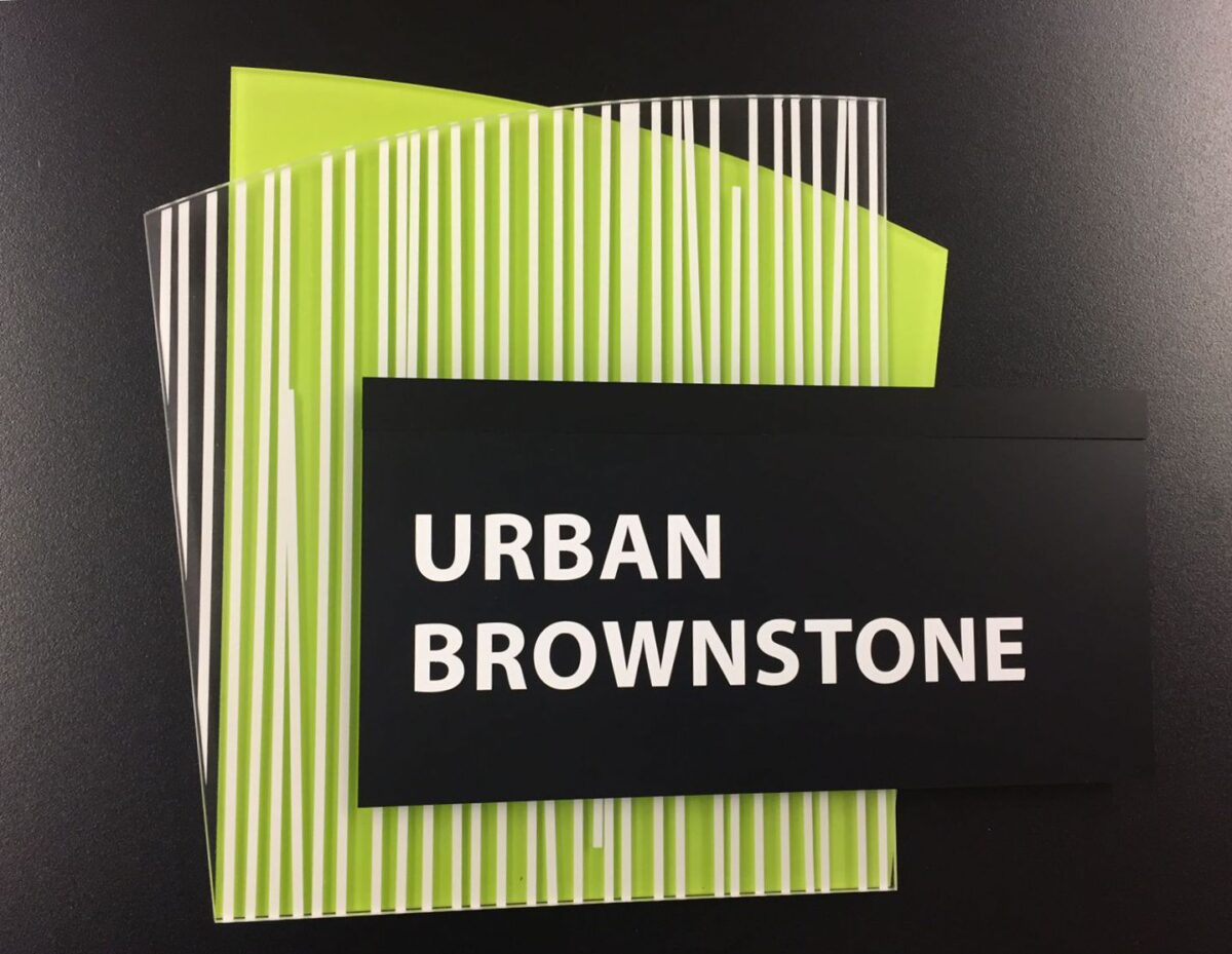 A rectangular black card with the text "URBAN BROWNSTONE" is placed on top of two lime green papers with black and white vertical stripes. The items are against a solid black background.