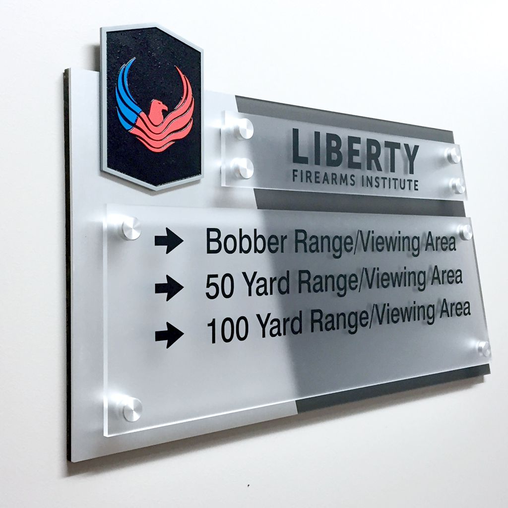 A wall-mounted sign with a black and red emblem at the top left, and "Liberty Firearms Institute" written next to it. Below, arrows point right to three different locations: "Bobber Range/Viewing Area," "50 Yard Range/Viewing Area," and "100 Yard Range/Viewing Area.
