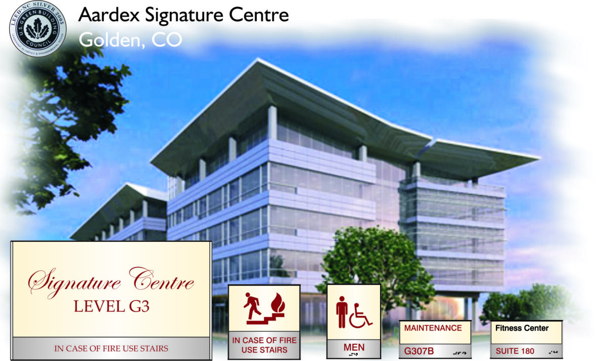 An image of the Aardex Signature Centre in Golden, CO. The building has a modern design with large glass windows. Signs below indicate directions for fire stairs, men's restroom, maintenance, Suite 180, and a fitness center. .