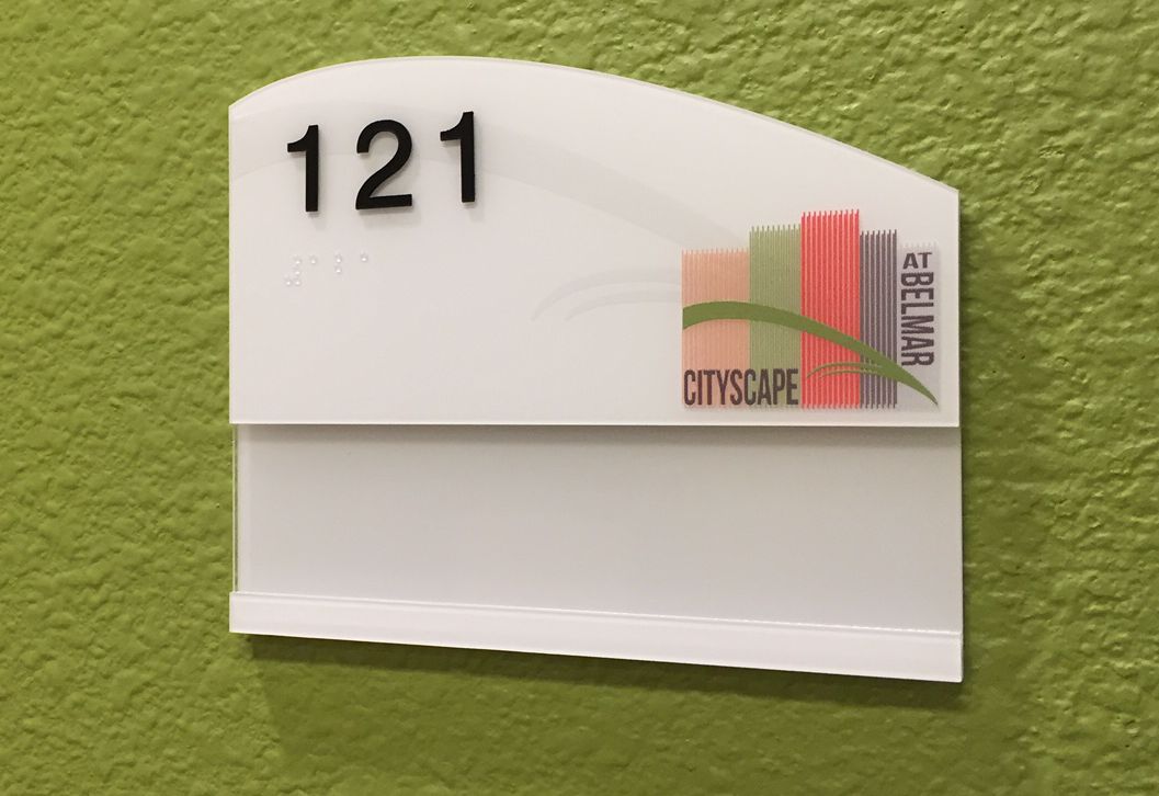 A green wall with a white, rectangular room number sign showing "121" in black text at the top. Below the number, there's a multicolored logo with abstract building shapes and the words “CITYSCAPE” on the right side.