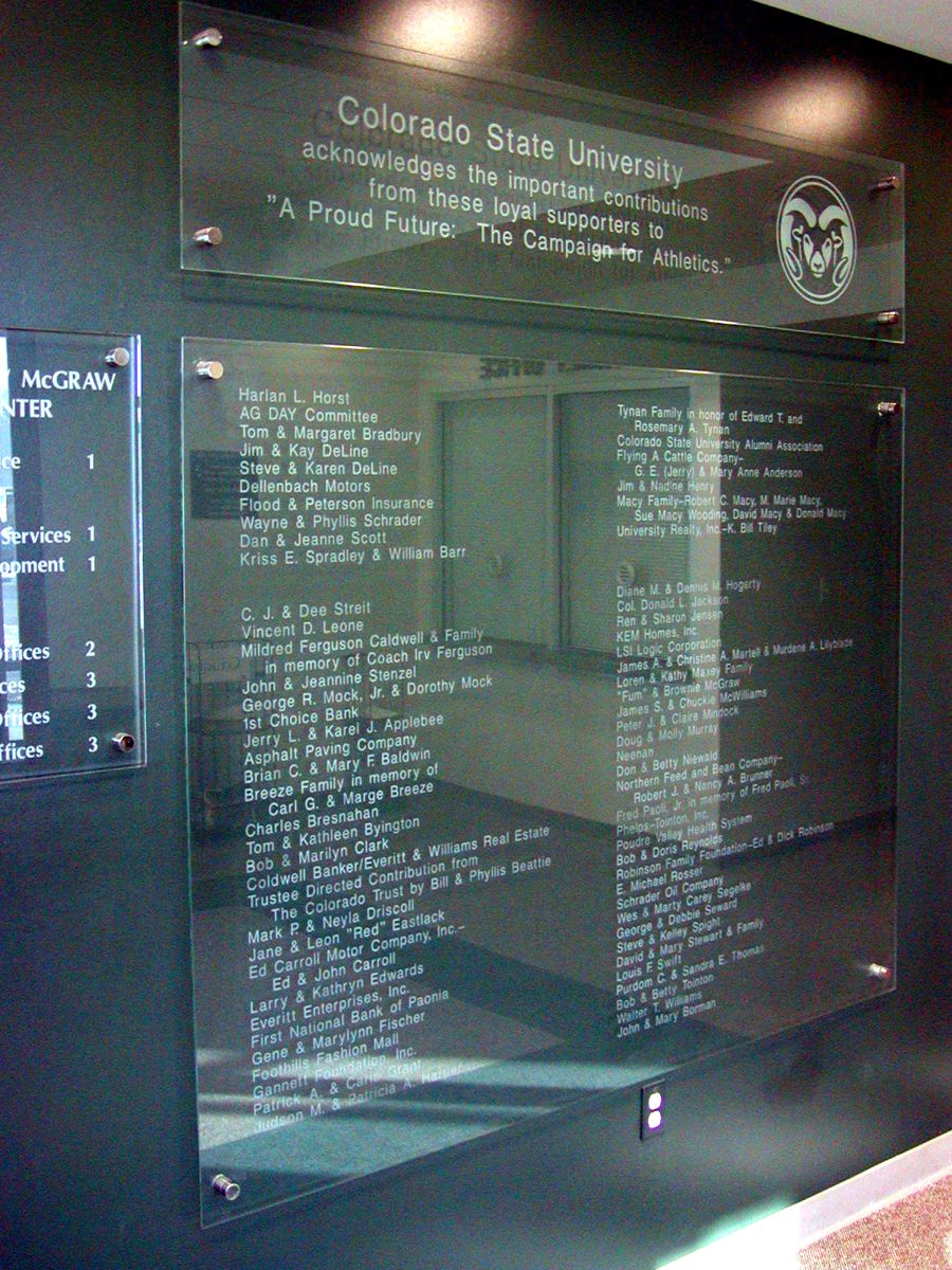 Glass donor recognition display at Colorado State University, showcasing names of individual and corporate benefactors. Etched text includes lists of contributors divided into sections, with the university logo visible at the top right corner.