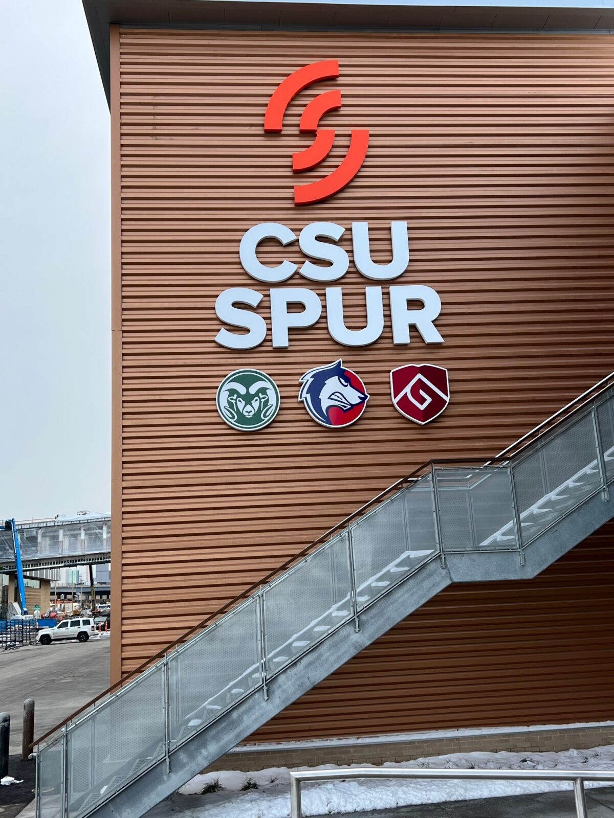 A modern building with large "CSU SPUR" sign and three illuminated logos on its facade.