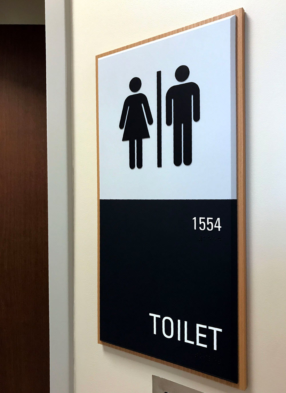 A sign indicating a restroom with male and female symbols. The sign is divided into two sections, with the top half displaying the symbols and the bottom half showing the room number "1554" and the word "TOILET" in white text on a black background.