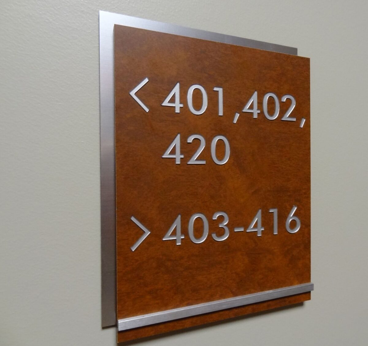 A wall-mounted sign with a brown background and silver edging displays room numbers: "< 401, 402, 420" for the left direction and "403-416" for the right direction.