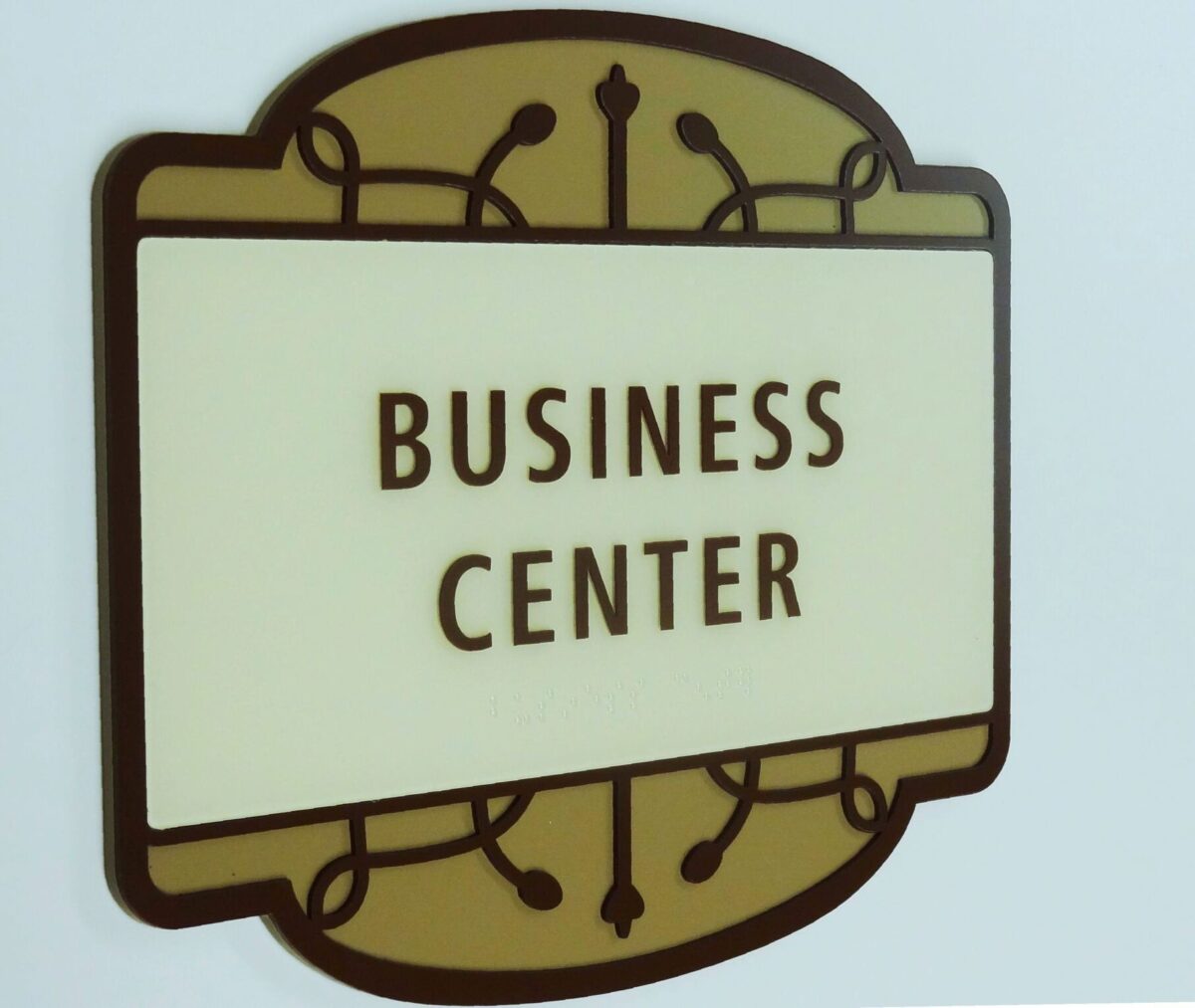 A rectangular sign with rounded corners, featuring decorative trim and the text "Business Center" in bold, brown letters against a light background. The design elements suggest a professional and formal setting.