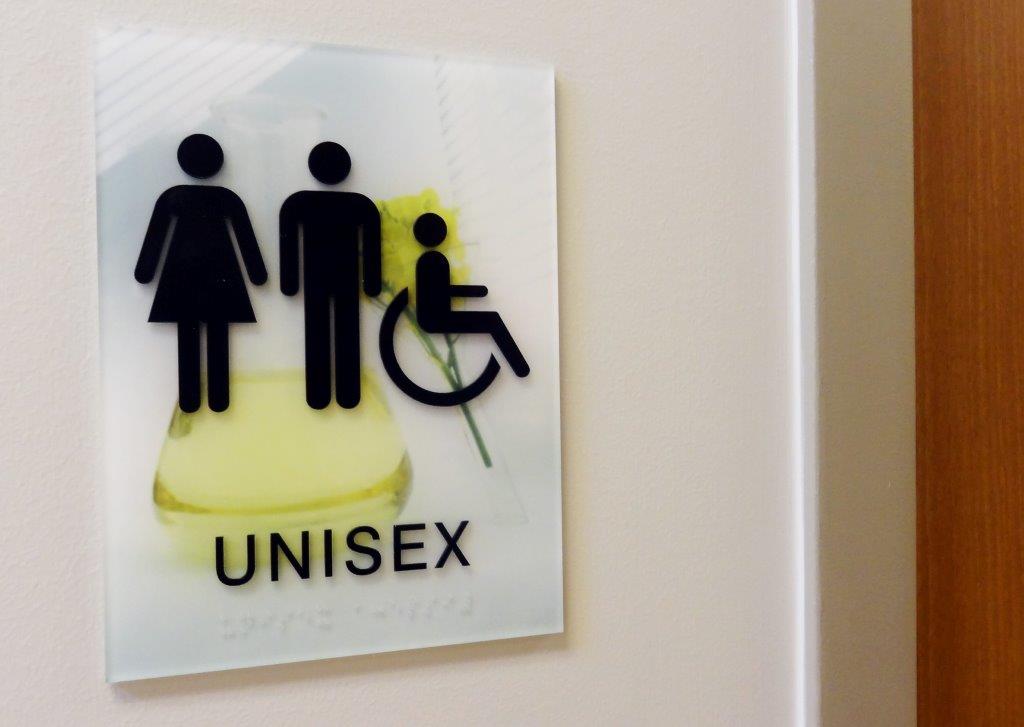 Sign on a wall labeled "UNISEX" with icons depicting a female figure, a male figure, and a person in a wheelchair, indicating an inclusive restroom.