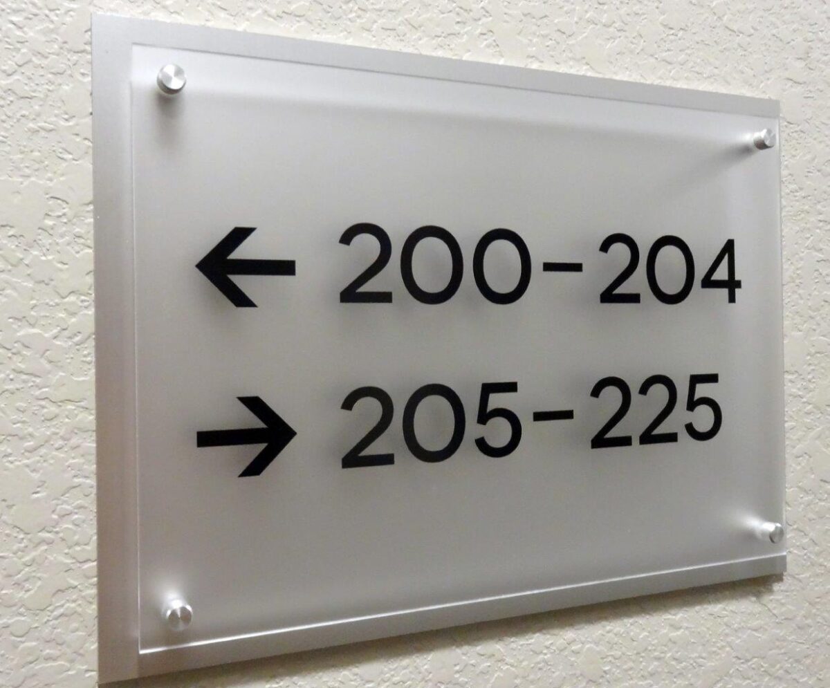 A frosted glass sign mounted on a wall indicates directions with black text: an arrow pointing left for rooms 200-204 and an arrow pointing right for rooms 205-225.
