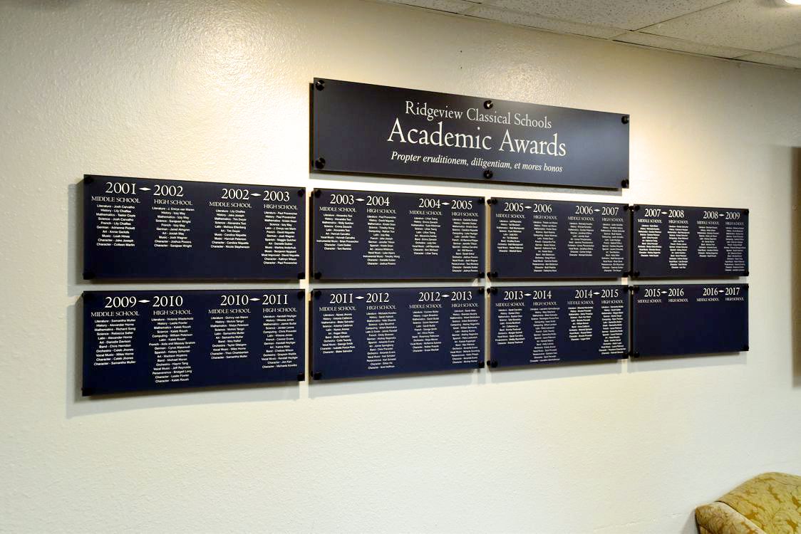 Plaques mounted on a wall display Ridgeview Classical Schools Academic Awards. Each plaque is titled with a school year and lists award recipients' names. The top plaque reads, "Ridgeview Classical Schools Academic Awards.