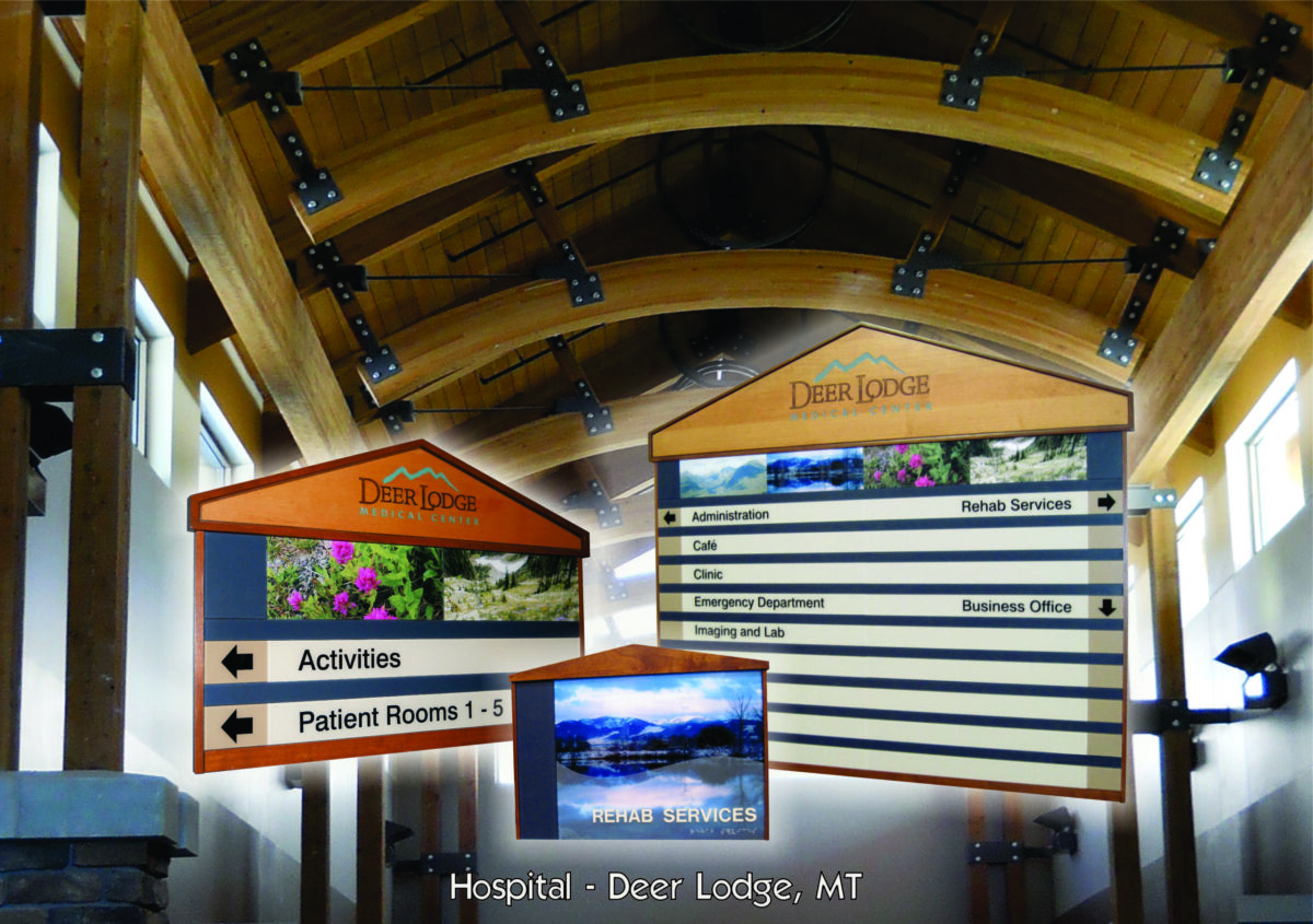 Wooden directional signs with text and images are displayed inside a building with a wooden arched ceiling and metal beams. The signs indicate locations for "Activities," "Patient Rooms 1-1," and various hospital services. Text at the bottom reads "Hospital - Deer Lodge, MT.