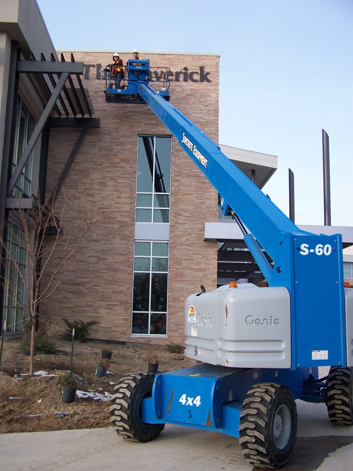 A blue Genie S-60 boom lift is extended to allow two workers to work on signage for the building.