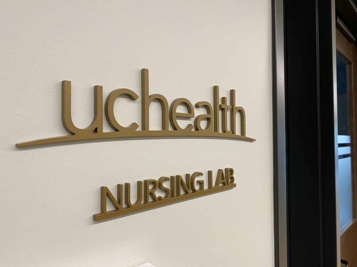 Wall sign reading "UCHealth Nursing Lab" in gold letters. The sign is affixed to a white wall near a dark-colored door frame.