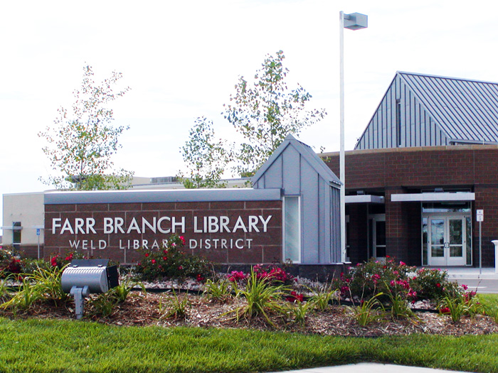 A modern library building with a sign reading "Farr Branch Library - Weld Library District" at the entrance. The building features a mix of brick and metal architecture, surrounded by well-maintained landscaping with flower beds and small trees.