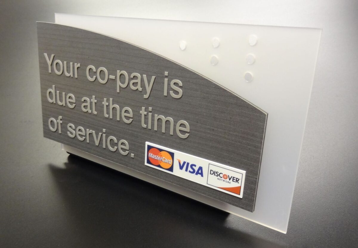 A sign with raised text reads, "Your co-pay is due at the time of service." At the bottom right, there are logos for MasterCard, Visa, and Discover, indicating accepted payment methods. The background is a frosted white with a gray section holding the text.