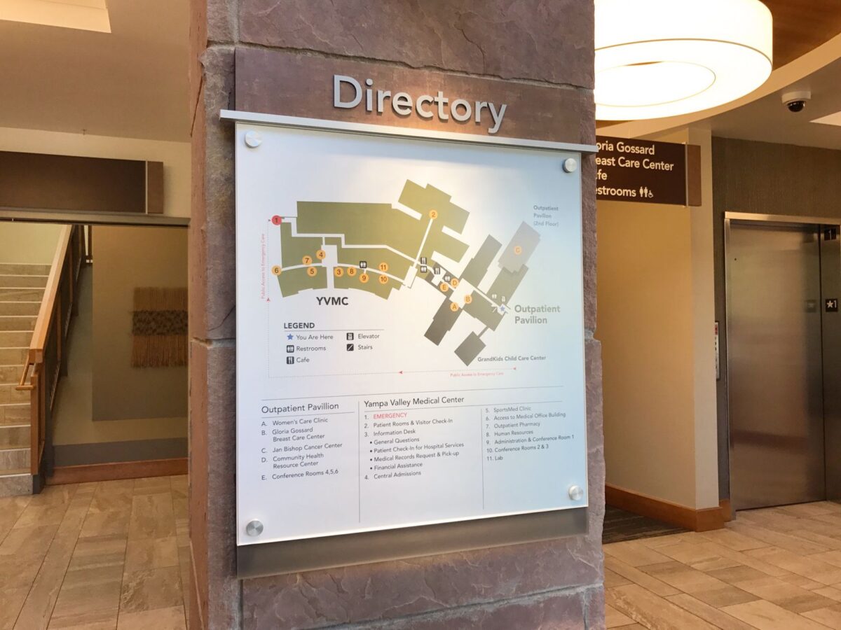 A building directory mounted on a wall, displaying a map and information about various locations within the building. The sign is labeled "Directory" and features floor plans and legend for easy navigation. The background includes stairs and an elevator.