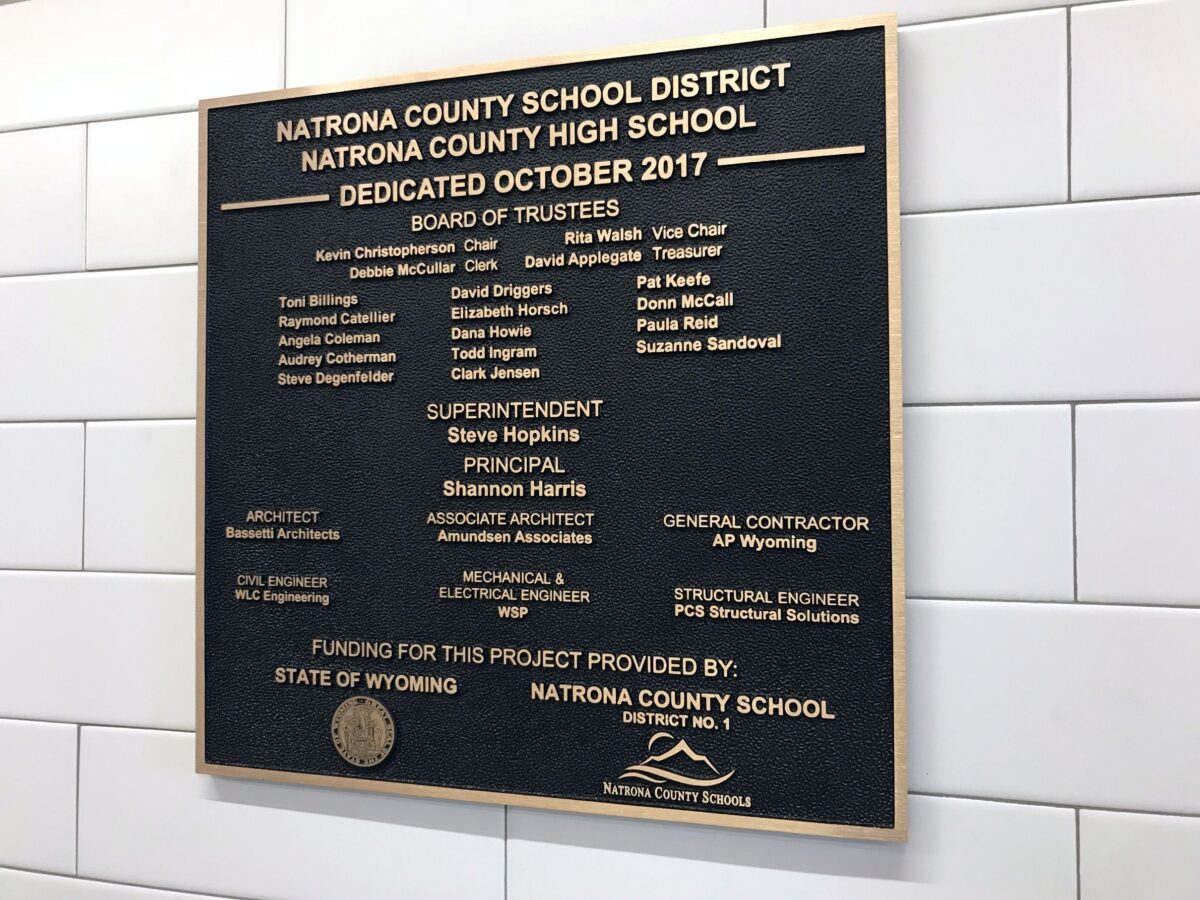 A bronze dedication plaque on a tiled wall reads, “Natrona County School District, Natrona County High School, Dedicated October 2017." It lists the Board of Trustees, Superintendent, Principal, Associate Principal, General Contractor, and Structural Engineer details.