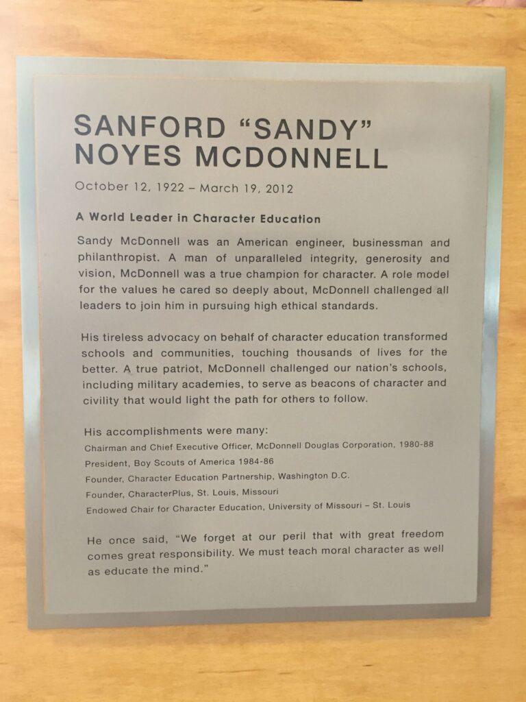 A plaque is dedicated to Sanford "Sandy" Noyes McDonnell, highlighting his contributions to character education. It details his leadership roles, awards, and philosophy on teaching moral character in schools. Dates of birth and death are October 12, 1922 - March 19, 2012.