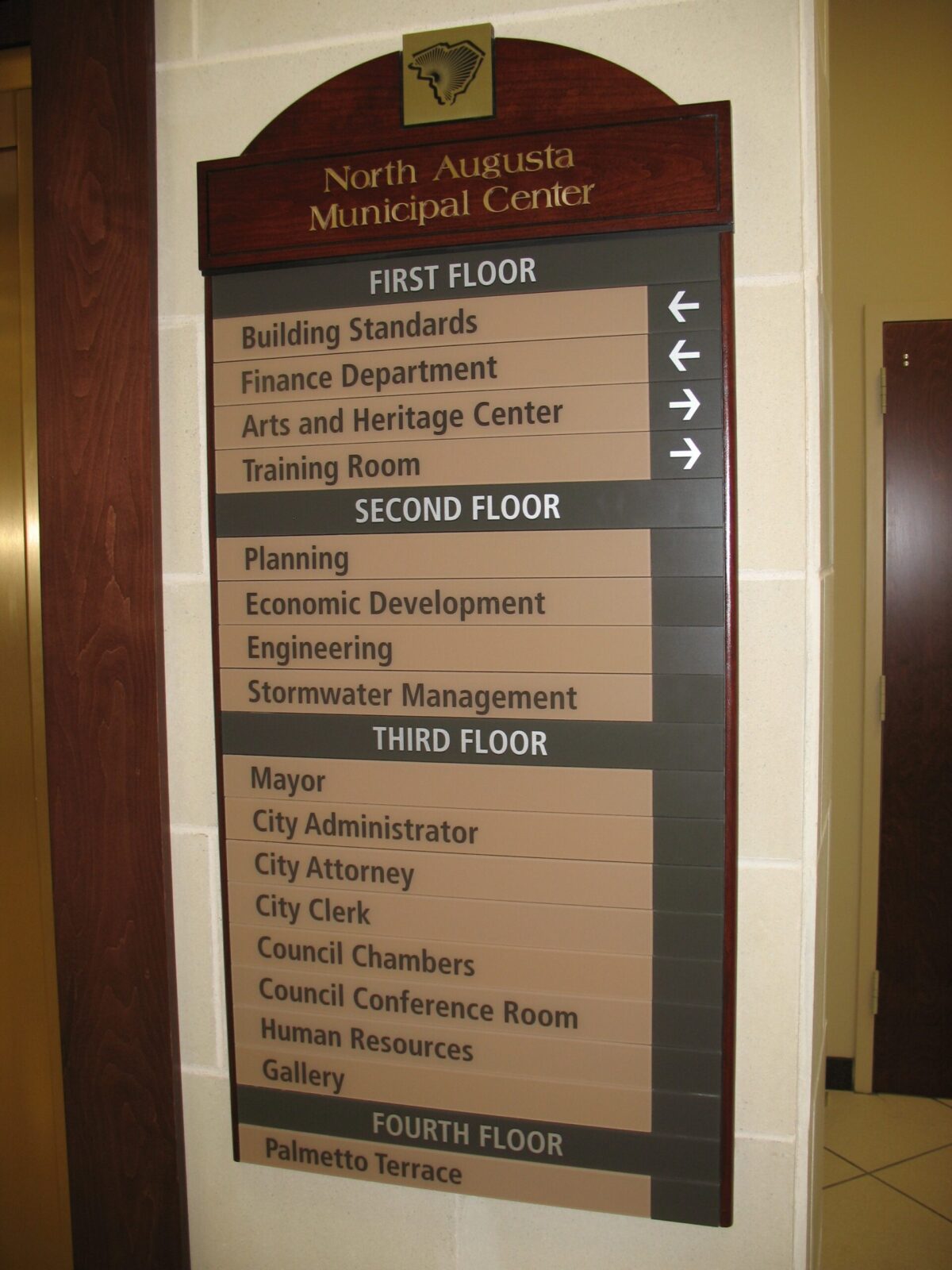 A directional sign inside the North Augusta Municipal Center listing various departments on different floors: Building Standards, Finance Department, Arts and Heritage Center, and Training Room on the first floor; Planning, Economic Development, Engineering, and Stormwater Management on the second floor; and Mayor, City Administrator, City Attorney, City Clerk, Council Chambers, Council Conference Room, Historical Resources, and Gallery on the third floor.