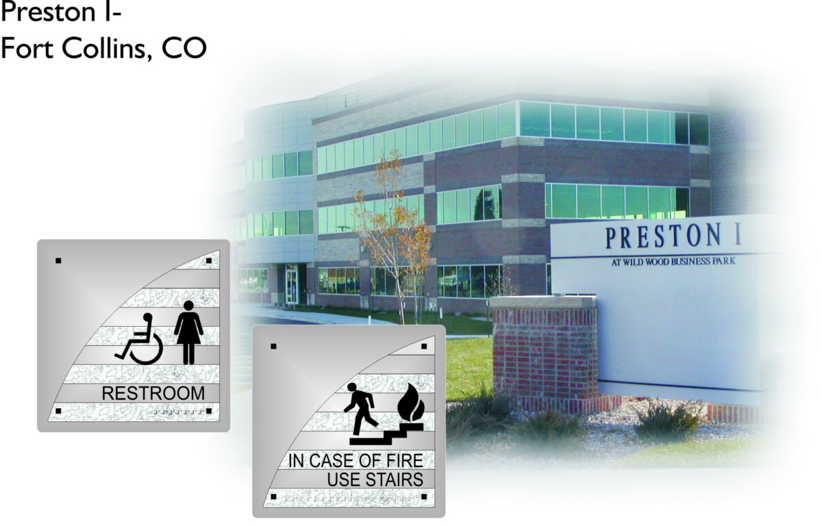 An image of a multi-story office building named Preston I located at Wild Wood Business Park in Fort Collins, CO. The scene includes foliage and a brick signpost. Two signs in the foreground indicate restroom accessibility and instructions for using stairs in case of fire.