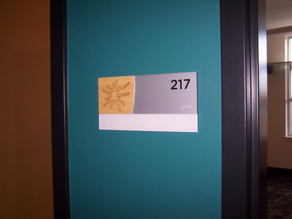 Office door number '217' with a wooden decorative element featuring a starburst design on a teal door.