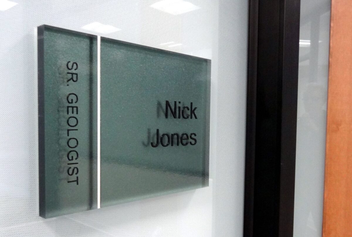Office nameplate reading "SR. GEOLOGIST" and "Nick Jones" on a frosted glass panel beside a door.